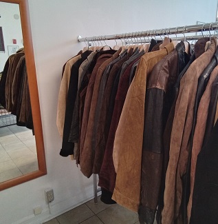 a row of suede jackets on a rack, part of a mirro on the wall is visible