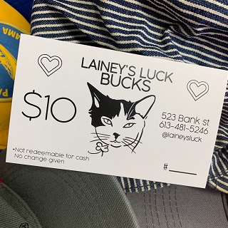 picture of a Lainey's Luck Bucks gift certificate that has the drawing of Lainey the cat in the middle, the address on the side (523 Bank St. 613-481-5246)